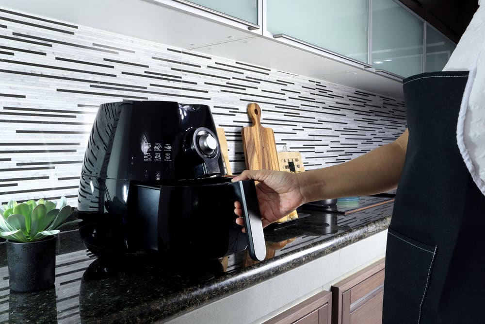 An Asian lady woman is holding the tray of the air fryer