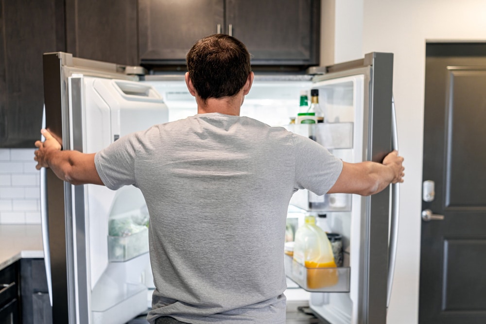 Back of hungry man opening fridge refrigerator doors