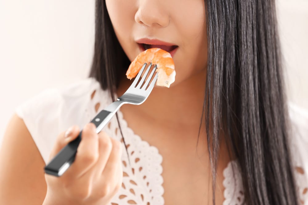 Beautiful young woman eating shrimp