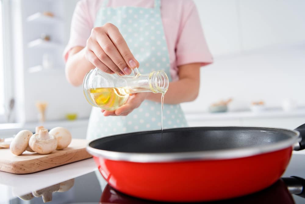 Cropped photo of beautiful housewife hold olive oil pouring hot frying pan