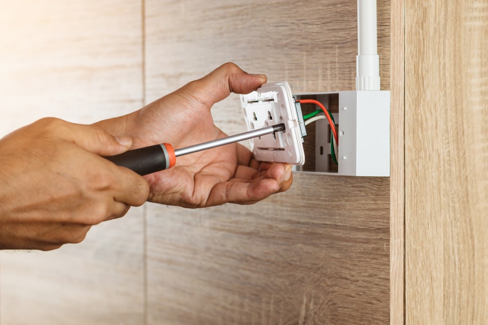 Electrician is using a screwdriver to install a power outlet in to a plastic box on a wooden wall