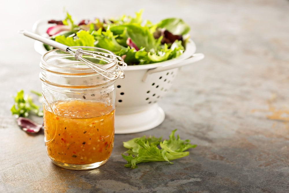 Italian vinaigrette dressing in a mason jar with fresh vegetables on the table