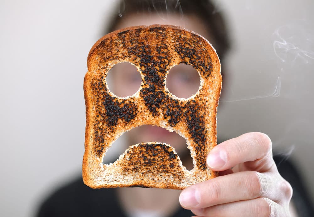 Man holding up a burnt slice of toast with an unhappy smiley concept