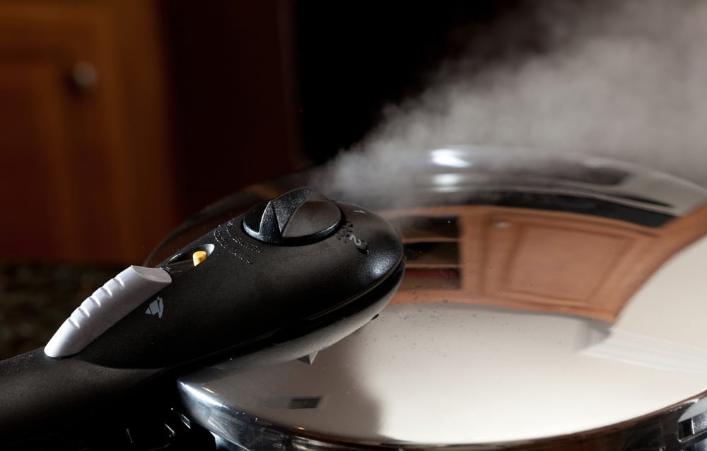 Steam escaping from lid of pressure cooker with reflection of modern kitchen