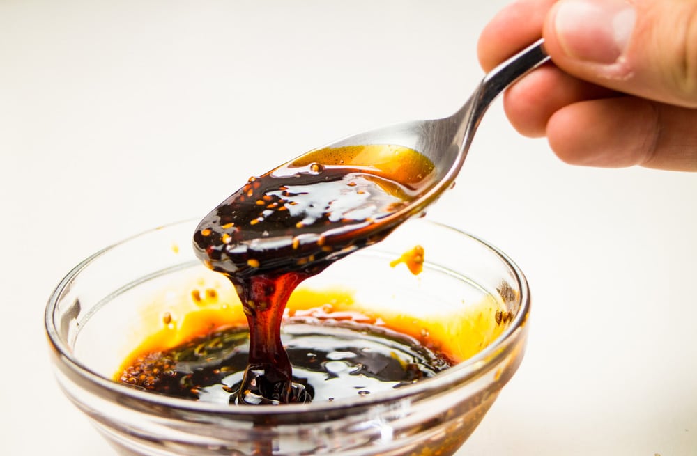 Thick teriyaki sauce dripping down from spoon into glass bowl 
