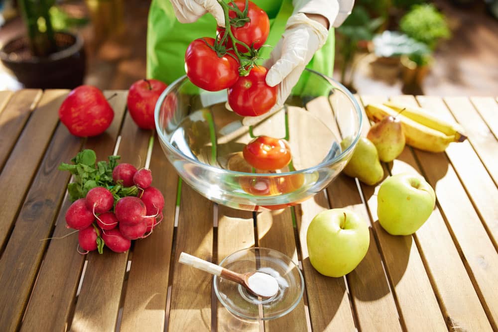 Woman in green apron removes pesticides by soaking vegetables and fruits in water with baking soda