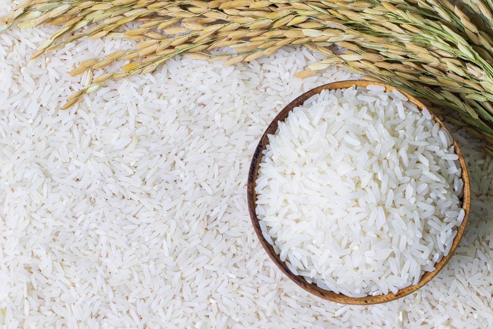 Wooden bowl with rice on rice and rice ears background