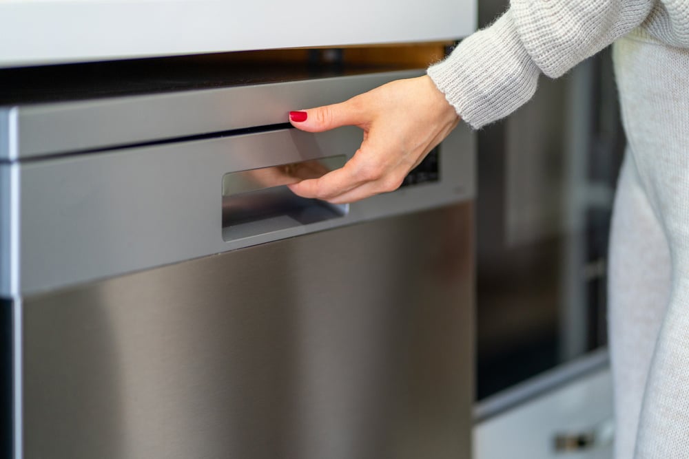 Young woman opening the dishwasher door with her left hand with red nail polish