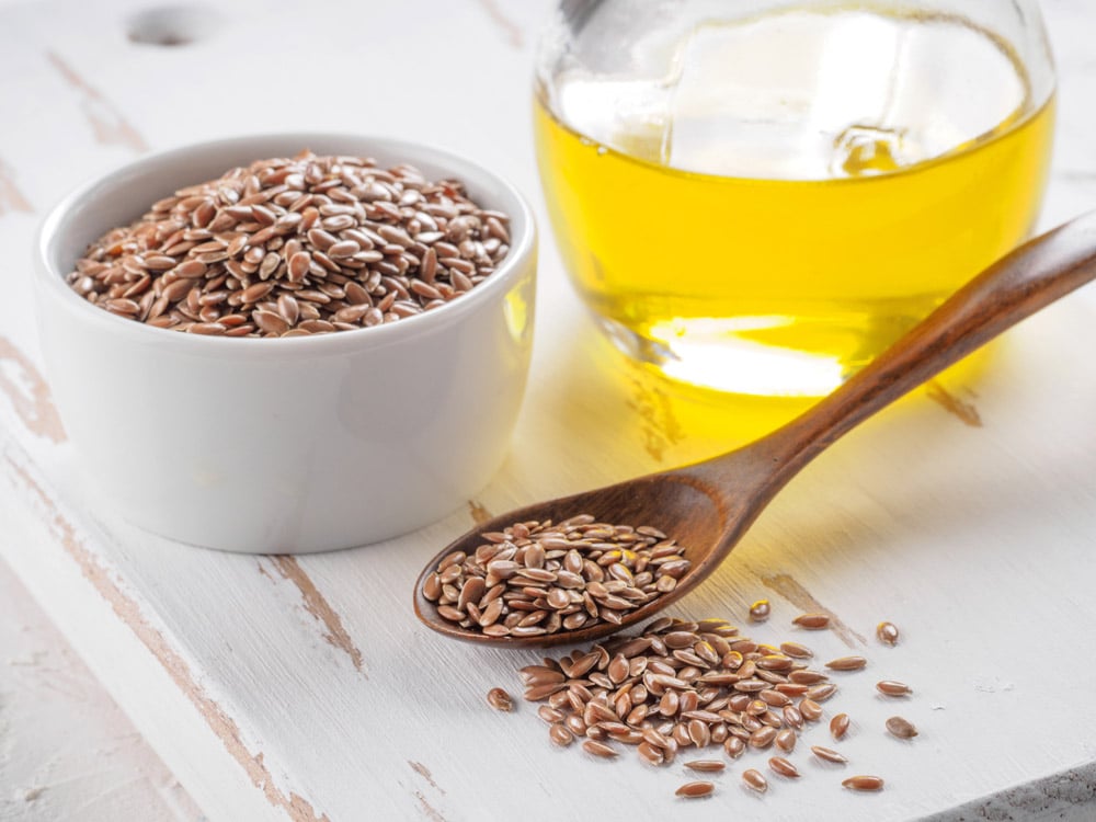 Brown flax seeds in spoon and flaxseed oil in glass bottle on white wooden background