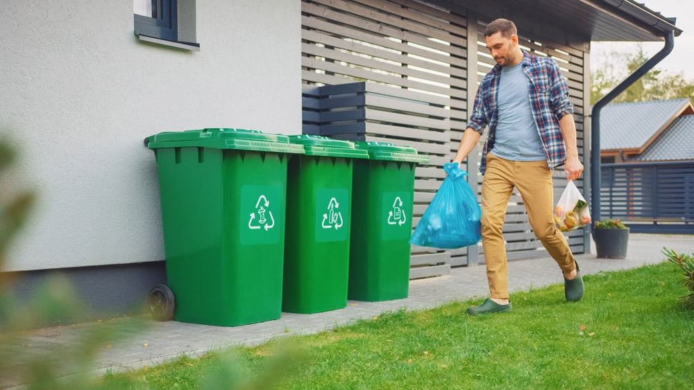 Caucasian Man is Walking Outside His House in Order to Take Out Two Plastic Bags of Trash