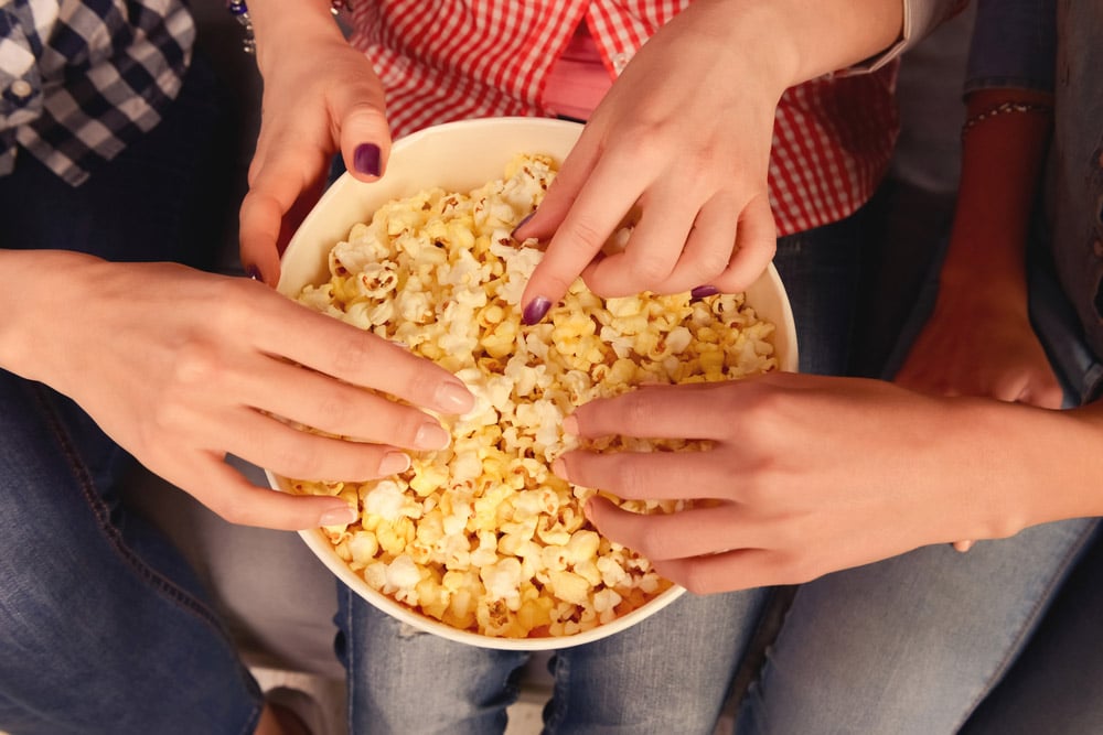 Top view photo of women's hands taking popcorn