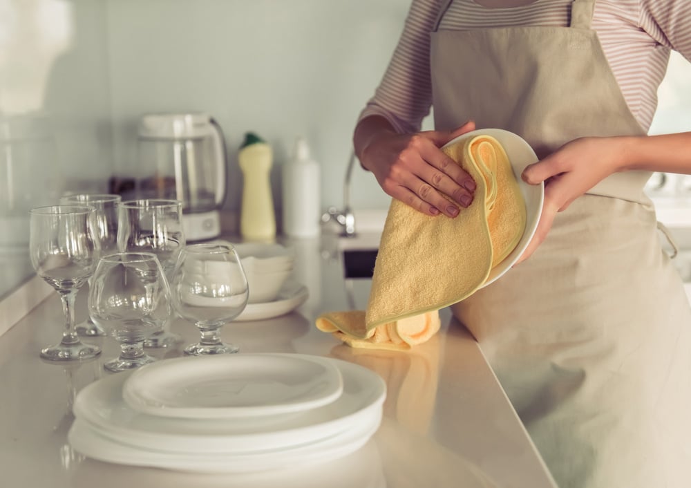 Cropped image of beautiful young woman in apron wiping the dishes in kitchen