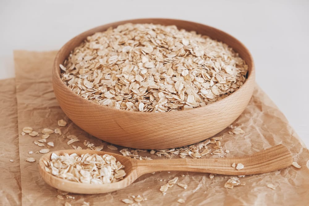 Dry oatmeal in a wooden bowl and spoon on kraft paper on a white background