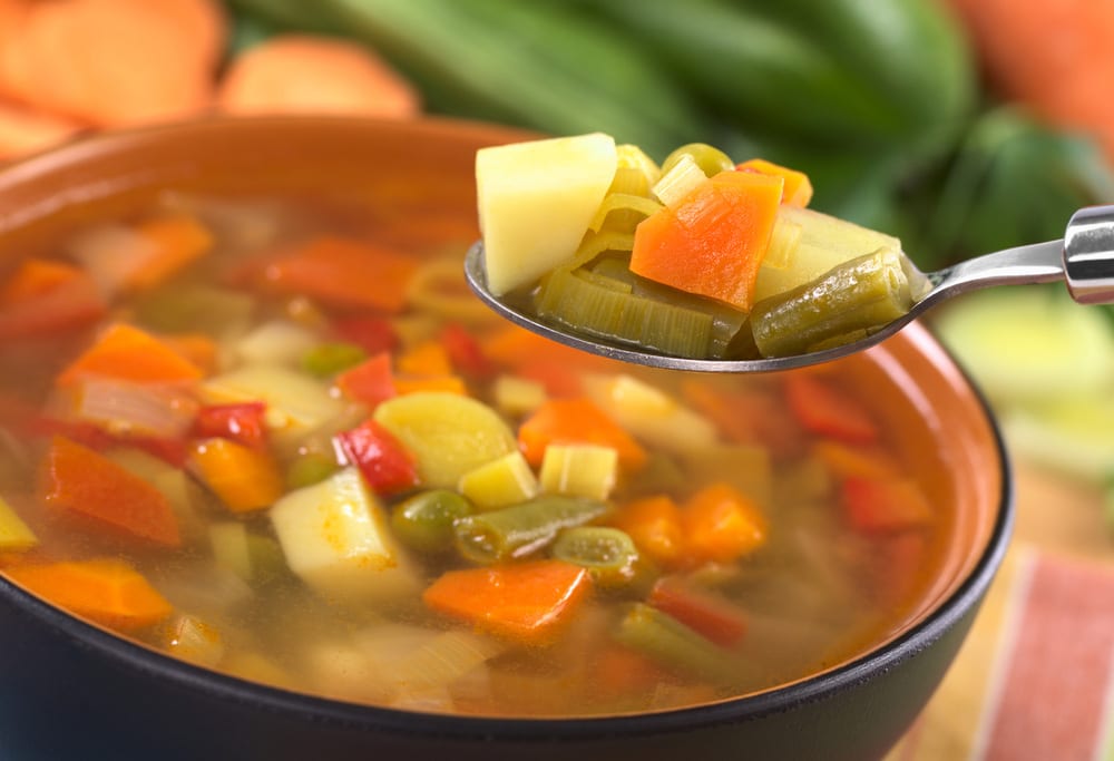 Fresh vegetable soup on spoon made of green bean, pea, carrot, potato, pepper, tomato and leek