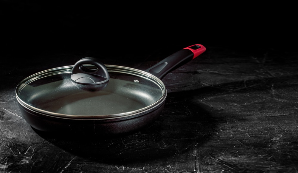A frying pan with a glass lid and a plastic handle on dark background