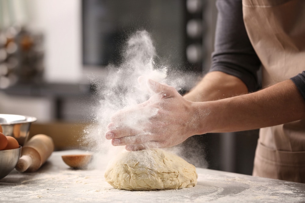 Male hands clapping and sprinkling white flour over dough