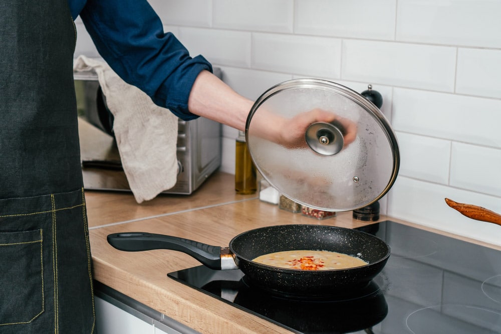Man holding glass lid of frying pan