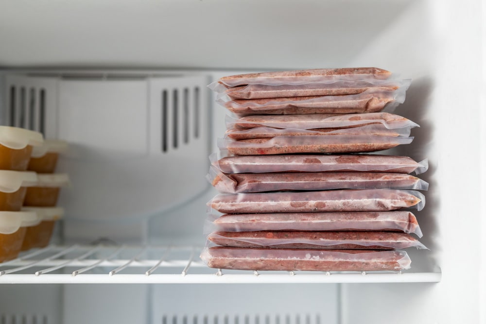 Many vacuum sealed frozen meat packages in a stack in the freezer