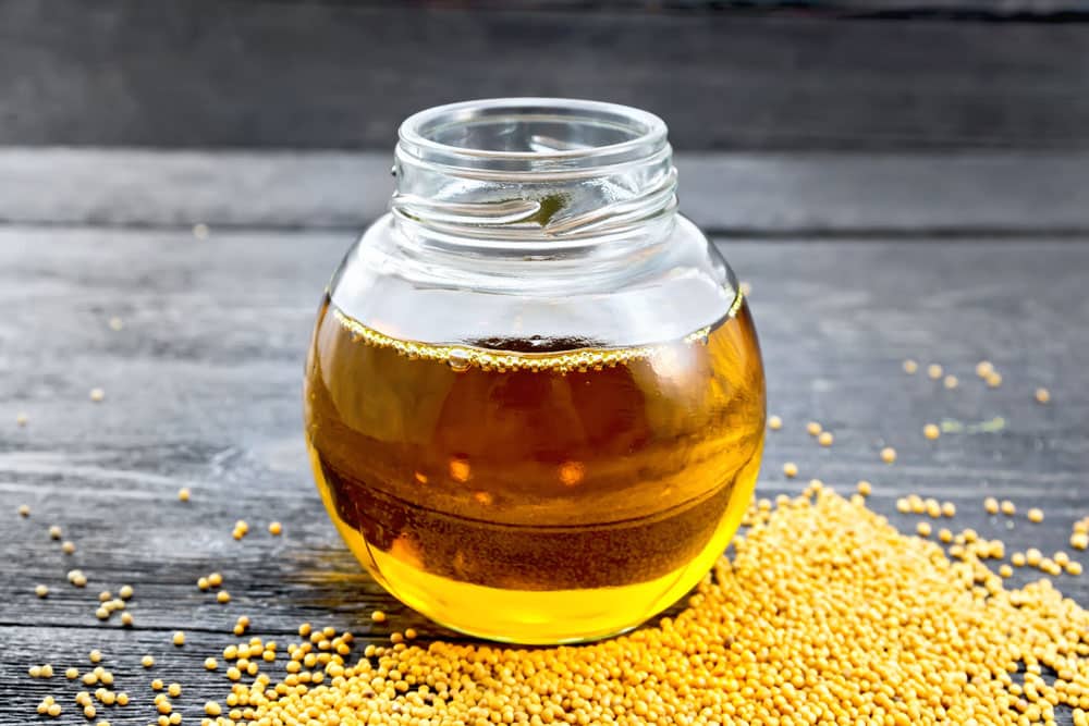 Mustard oil in a glass jar with seeds on a wooden board background