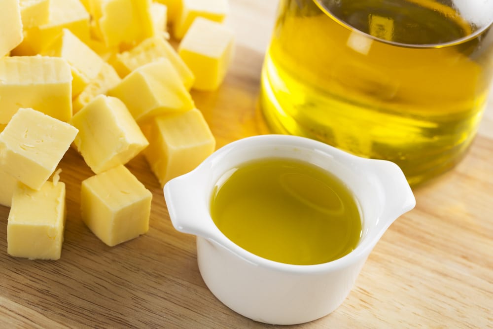 Olive oil in a small glass container with bottle of oil and cubes of butter