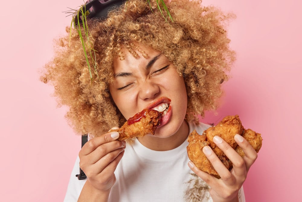 Photo of curly haired woman eats appetizing fried chicken nuggets with ketchup