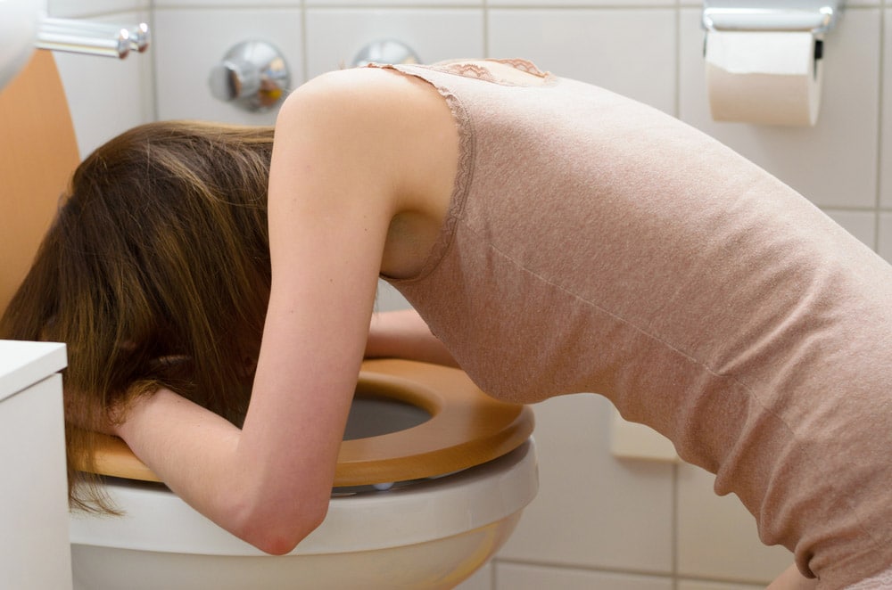 Side view on sick young woman wearing sleeveless shirt in leaning on open toilet seat
