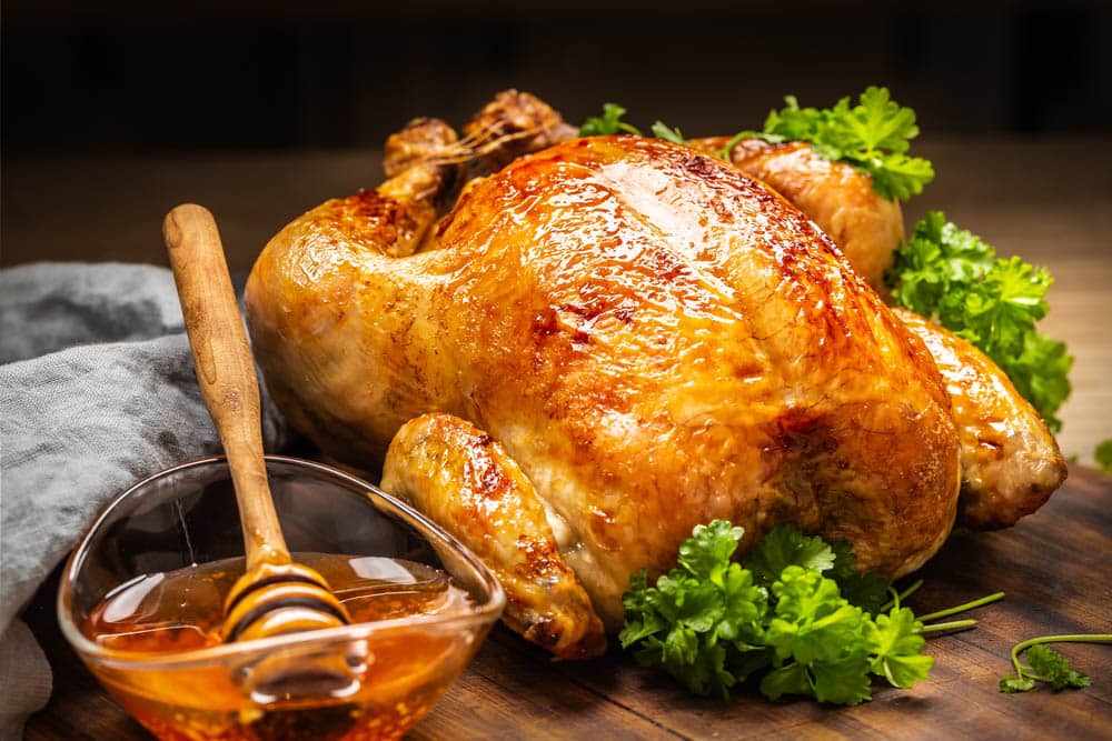 Whole baked chicken with crusty skin glazed with honey on top and parsley on the side