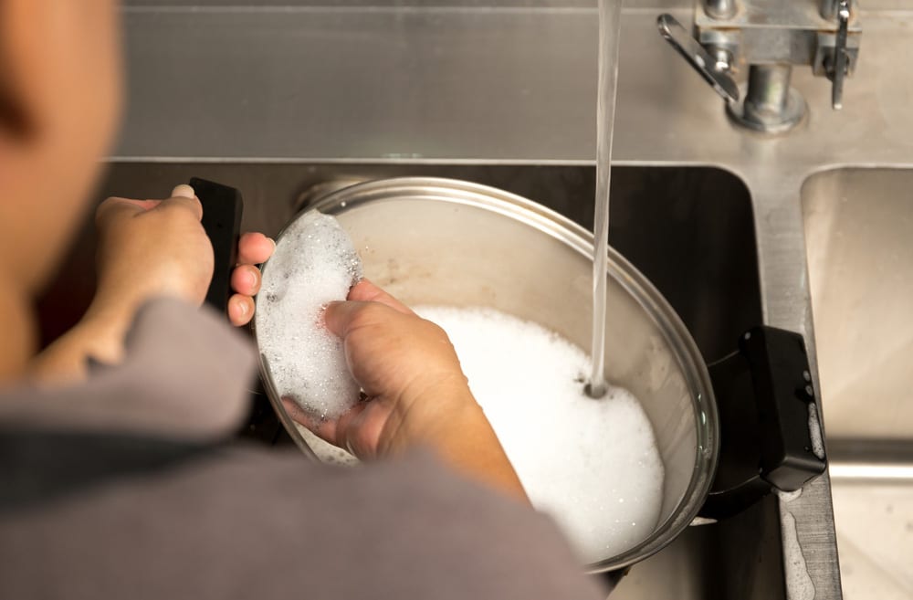 Woman hand washing stainless steel pot with dish washing soap in kitchen sink