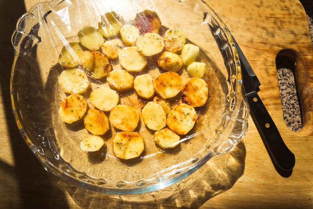 Baked potatoes in glass container covered with plastic