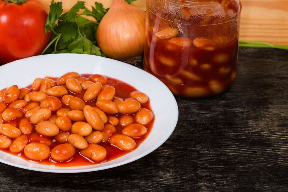Boiled beans stewed with tomato sauce on a white dish and in a glass jar