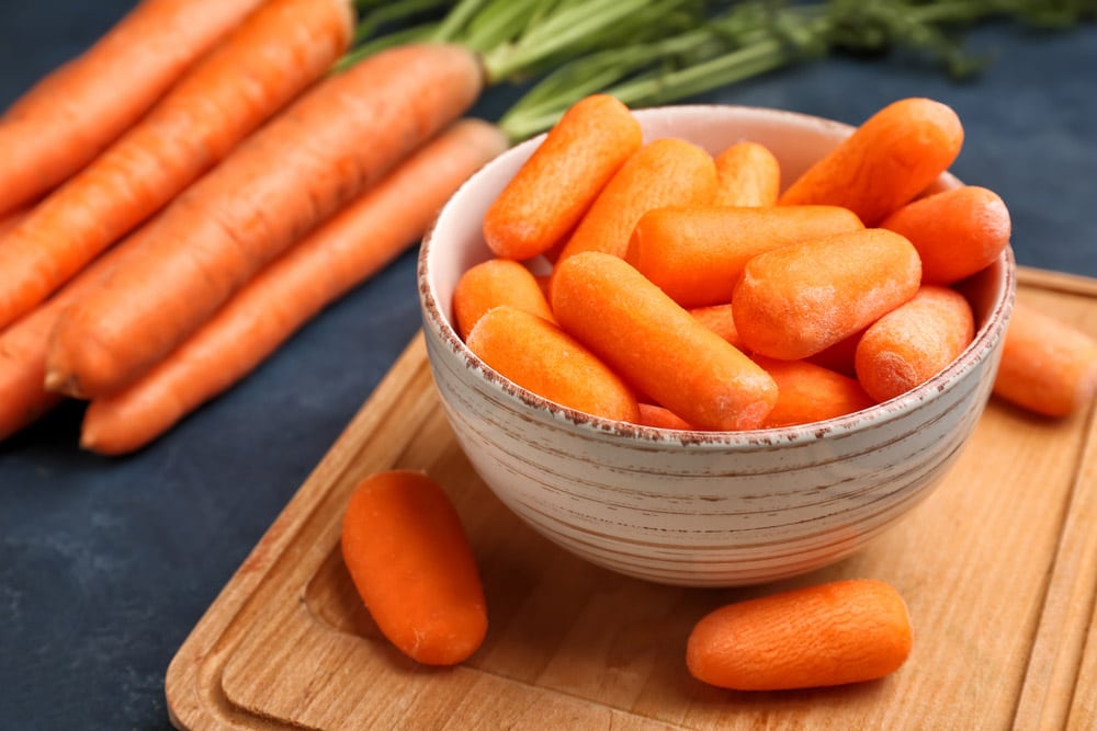 Bowl with fresh carrots on table