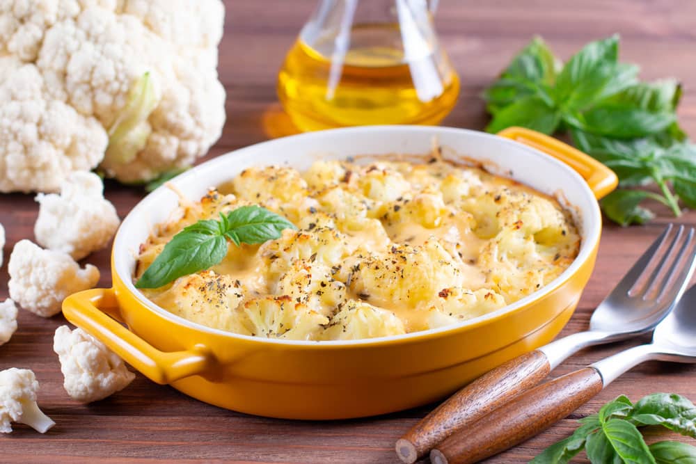 Cauliflower casserole with cheese and milk sauce in a baking dish on wooden table
