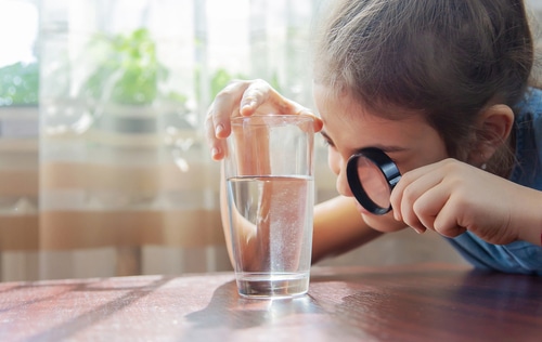 The child examines the water with a magnifying glass in a glass