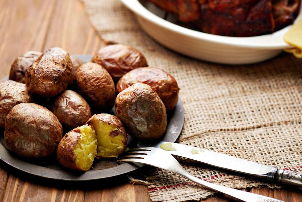 Close up at a plate of rustic roasted baked potato with knife and fork