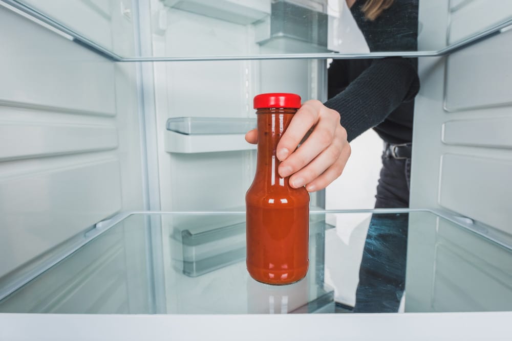 Cropped view of woman taking salsa sauce from refrigerator