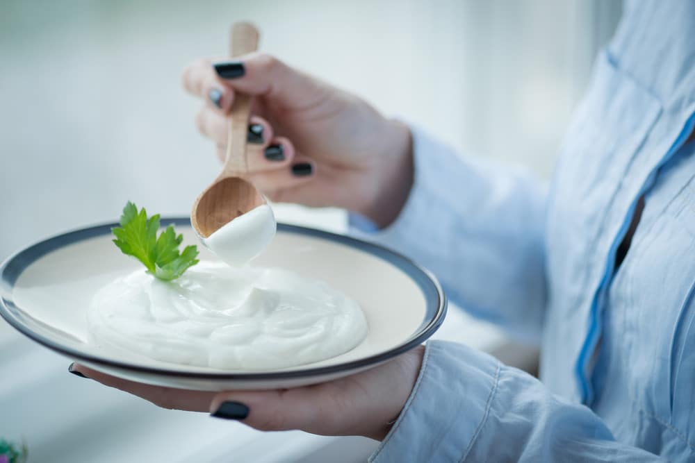 A cup of fresh sour cream in young woman's hands