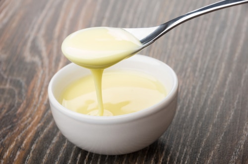 Glass bowl with sweet condensed milk and spoon with milk 