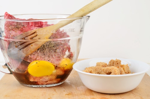 Hamburger meat, raw eggs and seasoning in clear glass mixing bowl