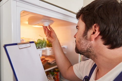 Handyman with checklist on clipboard checks lighting in refrigerator