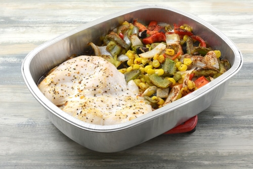 Hot two baked chicken breasts with corn, peppers, beans and onion vegetables in cooking pan on trivet