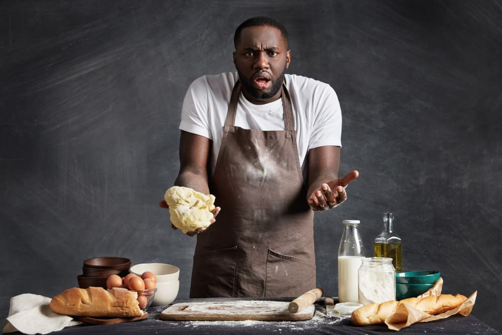 Indignant bewildered dark skinned male chef holds dough