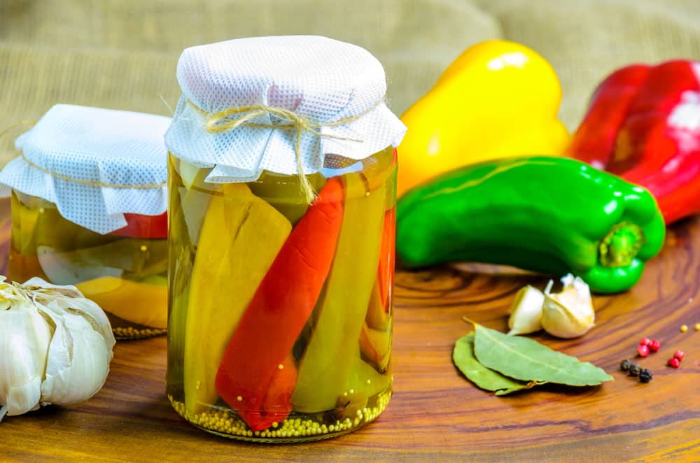 Canned red, green an yellow peppers in a jar on wooden background