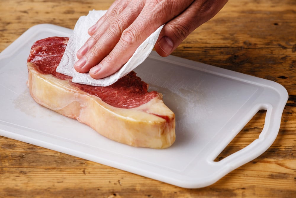 Raw fresh meat Steak Striploin on cutting board drying up excess moisture with paper towel