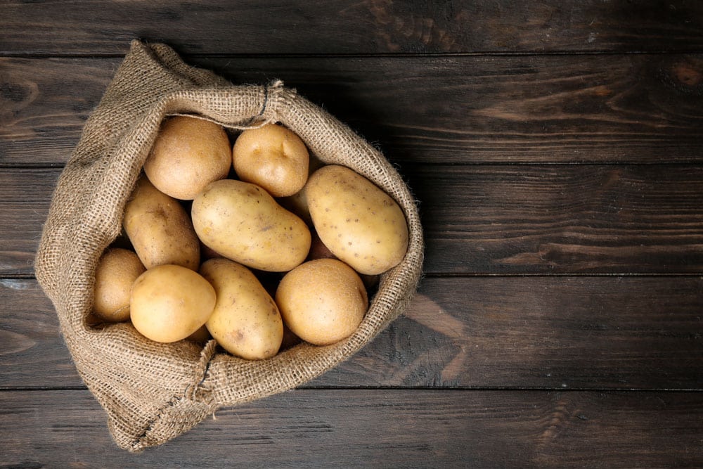 Sack of fresh raw potatoes on wooden background