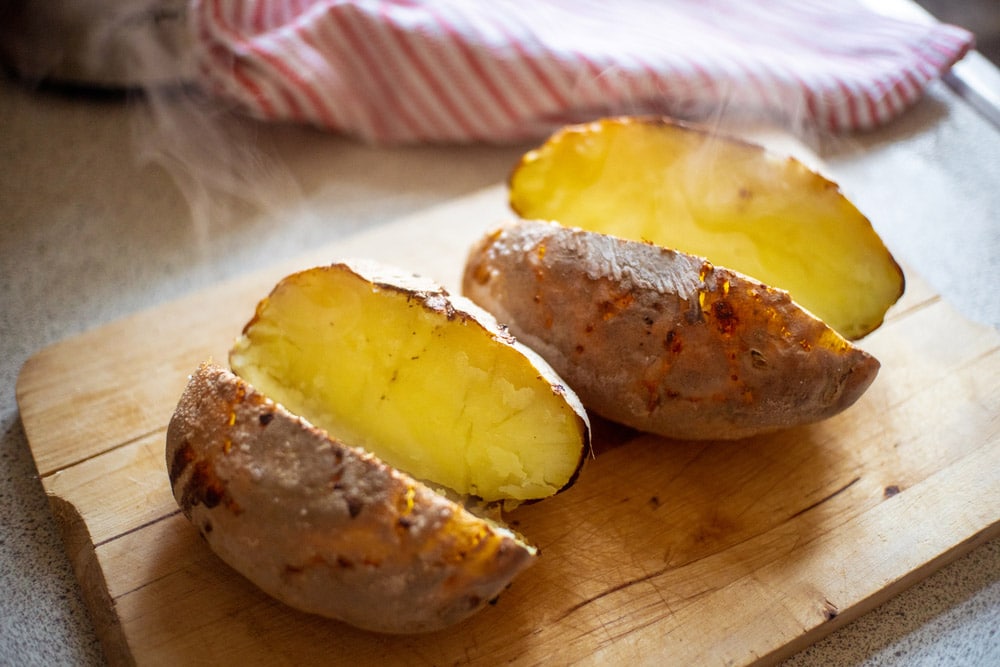 Steaming hot potatoes after oven roasting cut in half resting on wooden board