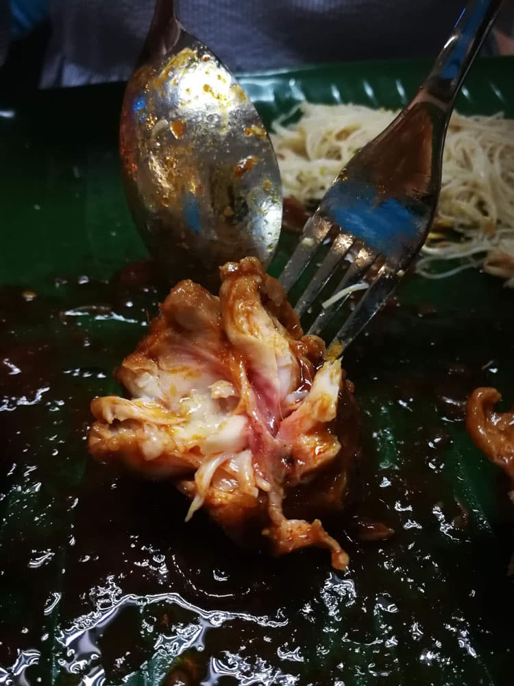 Undercooked chicken with raw flesh at inner part hold by fork and spoon