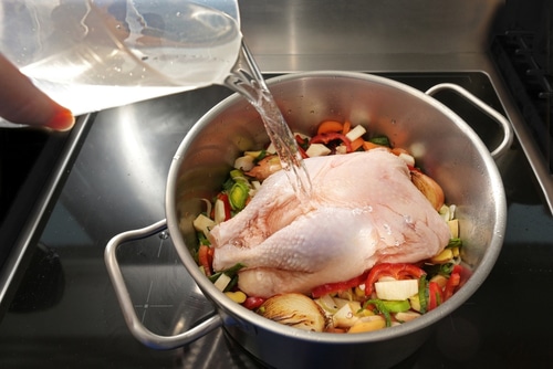 Whole raw chicken in a pot with chopped vegetables is poured with cold water