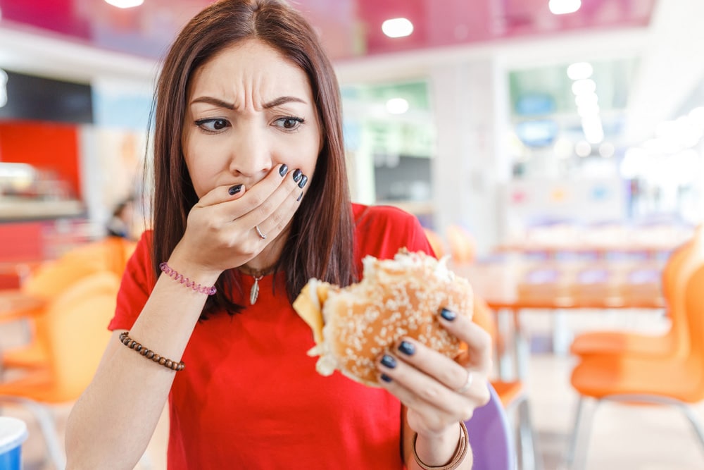 Woman with burger in hand, making bad and disgusting face