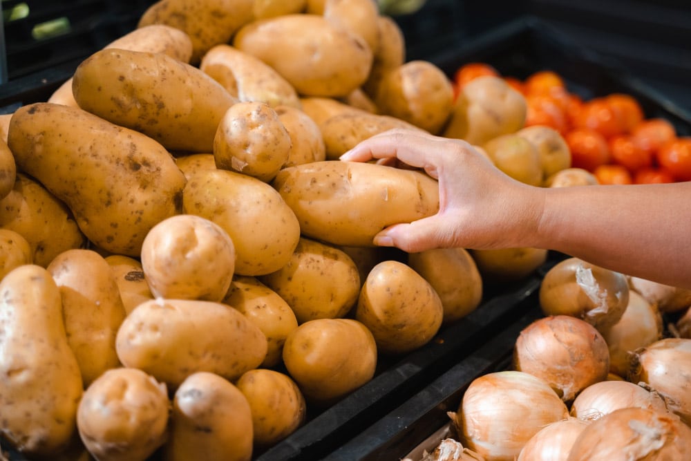 Woman hand picking up potato in supermarket