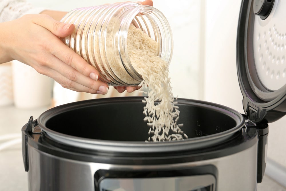 Woman pouring rice from jar into cooker in kitchen
